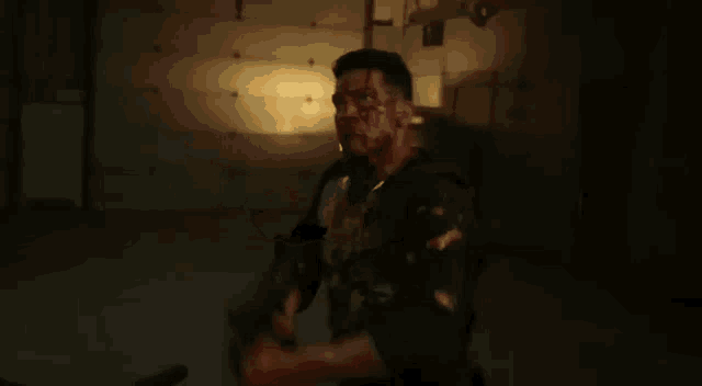 a man with blood on his face is holding a gun in a dark room and shooting it .