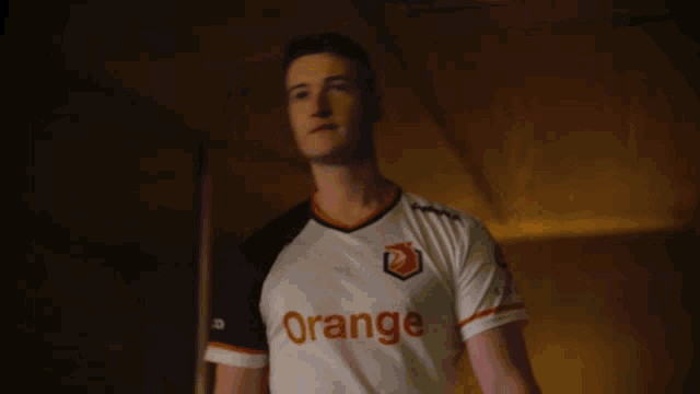 a man wearing an orange shirt stands in the dark