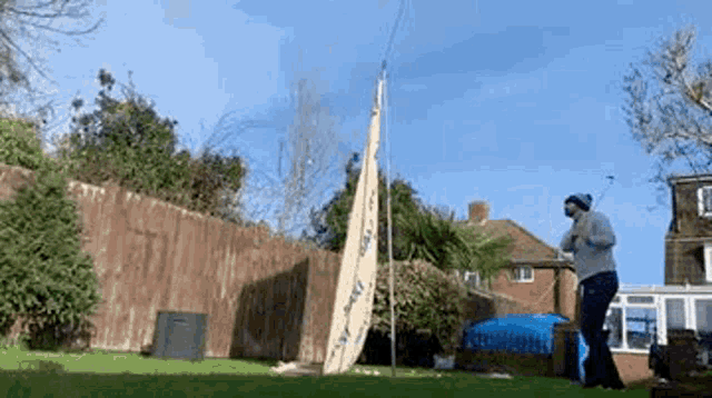 a man is standing in a backyard with a surfboard in the background .