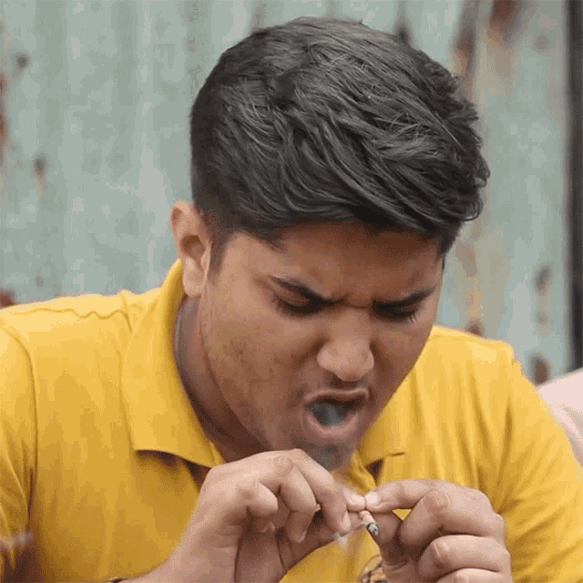a man wearing a yellow shirt is smoking a cigarette