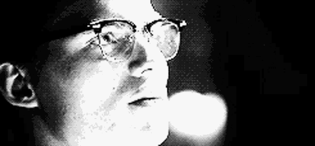 a close up of a man wearing glasses in a black and white photo