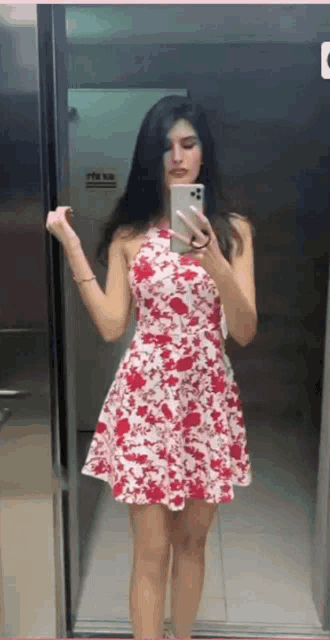 a woman in a red and white floral dress is taking a picture of herself in an elevator