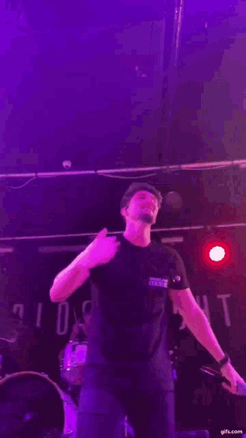 a man is singing into a microphone on a stage in front of a drum set .
