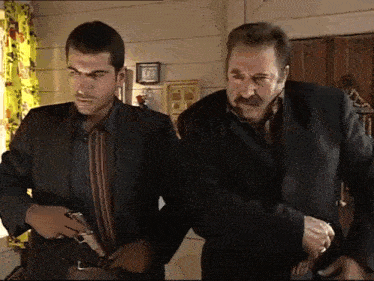 two men are standing next to each other in a room and one is holding a gun