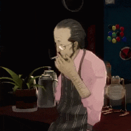 a man in a pink shirt and apron is sitting at a table with his hands folded
