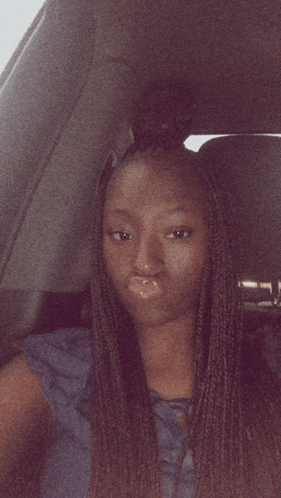 a woman with braids is sitting in a car and making a face