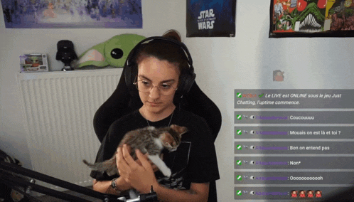 a woman wearing headphones is holding a kitten in front of a star wars poster