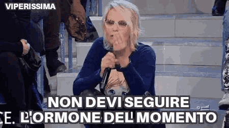 a woman is sitting on a staircase holding a microphone and saying non devi seguire l' ormone del momento .