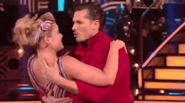 a man in a red shirt is hugging a woman in a striped dress