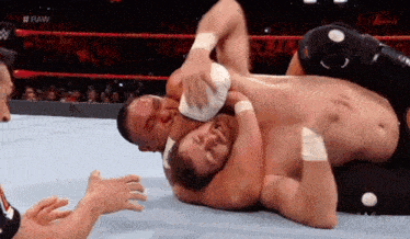 two men are wrestling in a wrestling ring while a referee looks on .