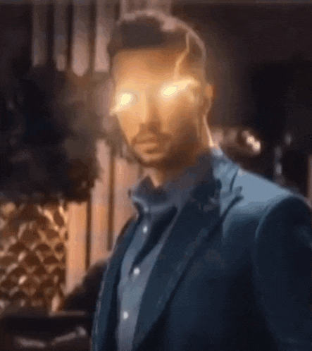 a man in a suit and blue shirt is standing in a room with his eyes glowing .