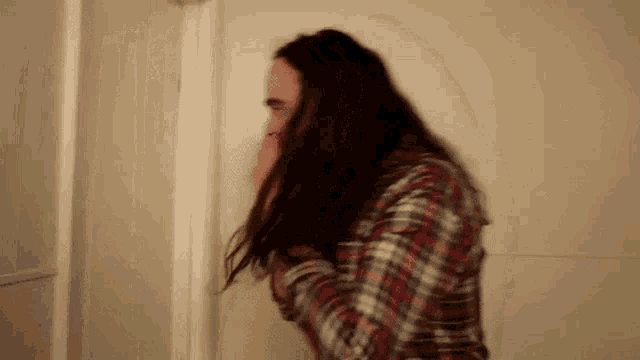 a woman with long hair is standing in front of a door covering her face .