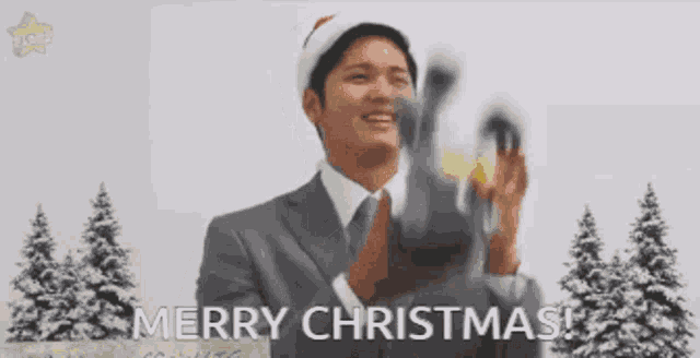 a man in a suit and tie is wearing a santa hat and saying merry christmas