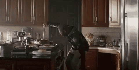 a man in a black jacket is standing in a kitchen looking at plates on the counter .
