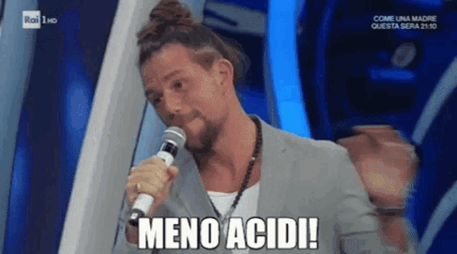 a man is singing into a microphone with the words meno acidi below him