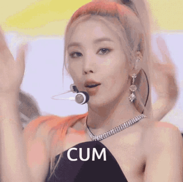 a woman wearing a necklace and earrings says cum in front of a microphone