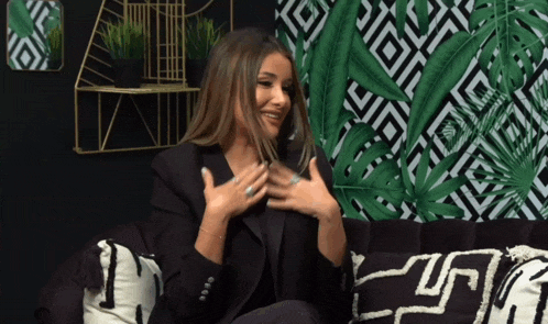 a woman is sitting on a black couch with a greek key pattern on the wall behind her
