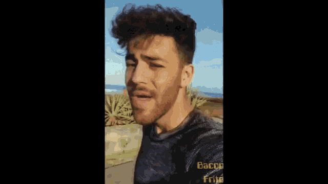 a man with a beard is smiling and wearing a black shirt that says bacon