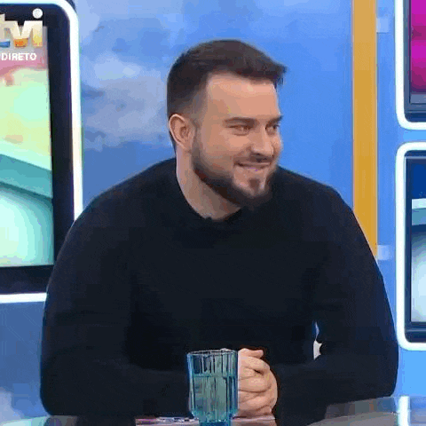 a man with a beard is sitting at a table holding a glass of water .