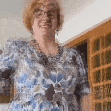 an elderly woman wearing glasses and a blue dress is standing in a room .