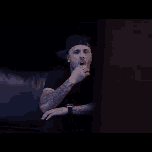 a man wearing a hat and a watch is sitting on a couch with his mouth open