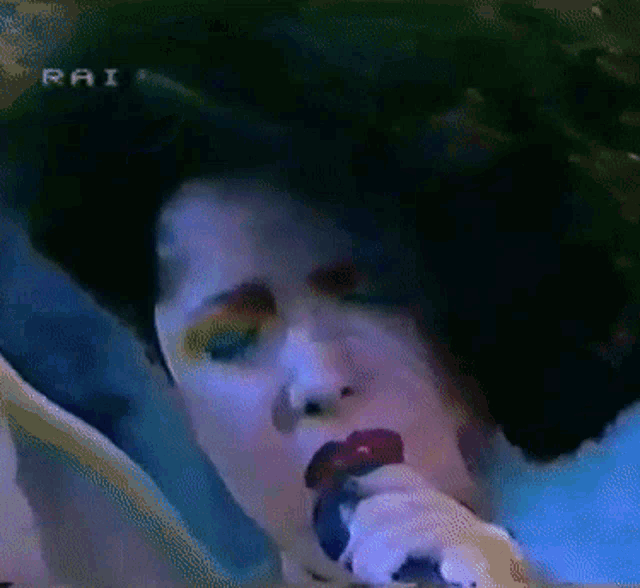 a woman singing into a microphone with rai written on the bottom of the screen