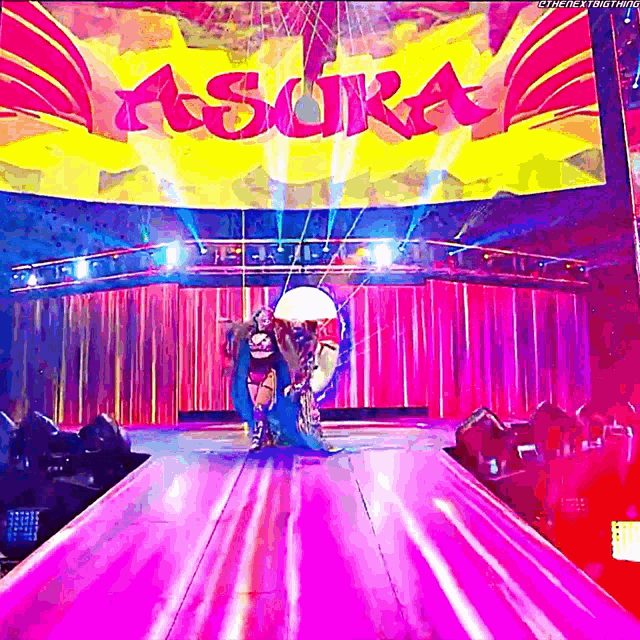 a woman in a wheelchair is walking down a stage with a large screen behind her that says asora