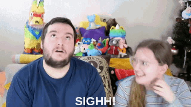 a man and a woman are sitting in front of stuffed animals and a sign that says sighh on it