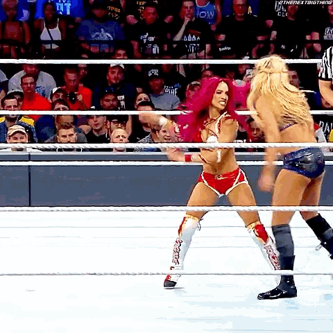 two women are wrestling in a ring with a referee in the background .