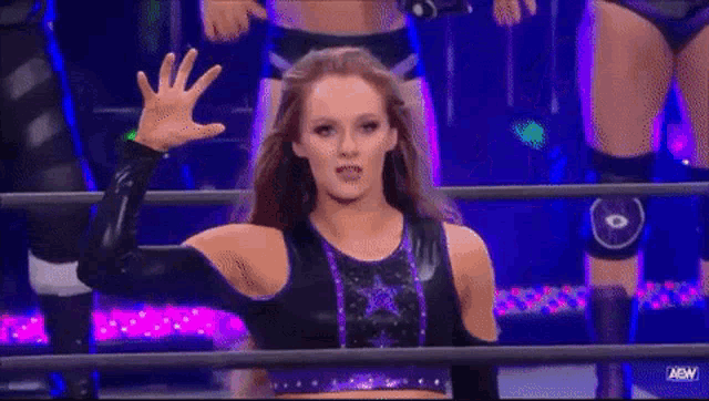 a female wrestler is waving her hand in the air while standing in a ring .