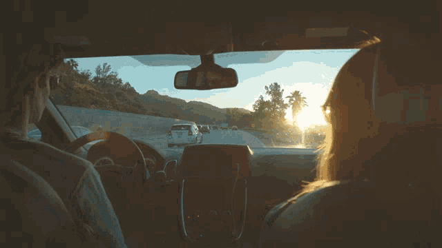 a man and a woman are driving down a highway and the sun is shining through the windshield