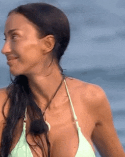 a woman in a bikini is standing in front of the ocean .