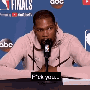 a man is sitting in front of a microphone with a sign that says f * ck you ..