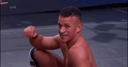 a shirtless wrestler is sitting on the floor with his fist in the air .
