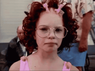 a girl with curly red hair and glasses is making a funny face .
