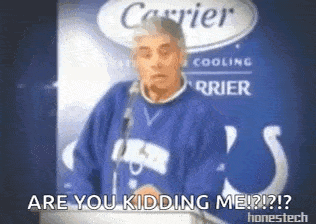 a man in a blue sweater is standing in front of a carrier sign .