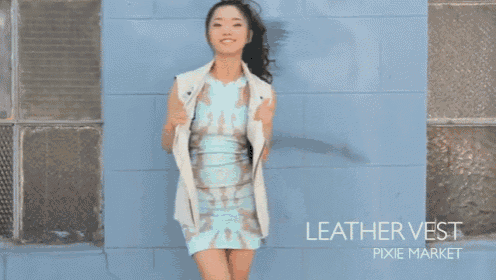 a woman standing in front of a blue wall wearing a leather vest