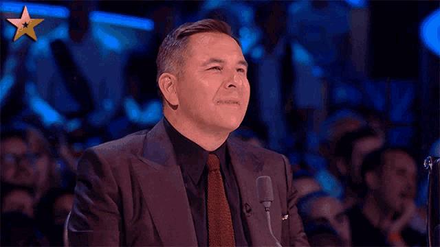 a man in a suit and tie is sitting in front of a microphone and smiling