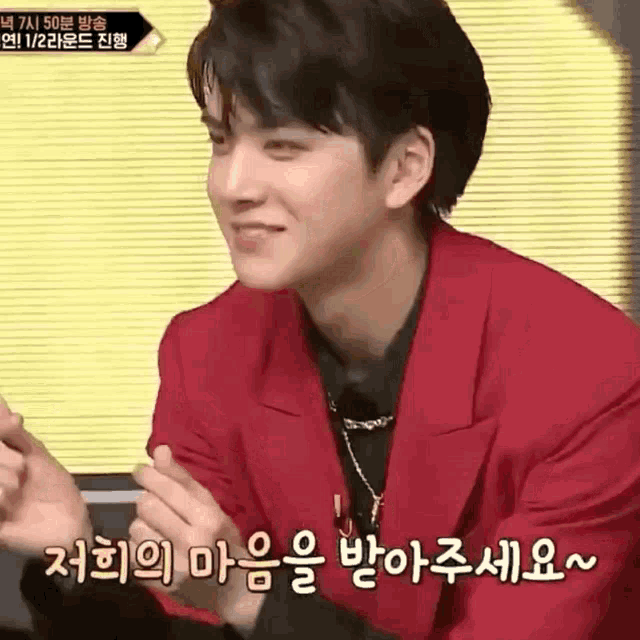 a young man in a red jacket is smiling with korean writing on his face .