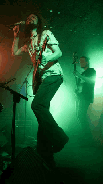 a man singing into a microphone while another man plays guitar