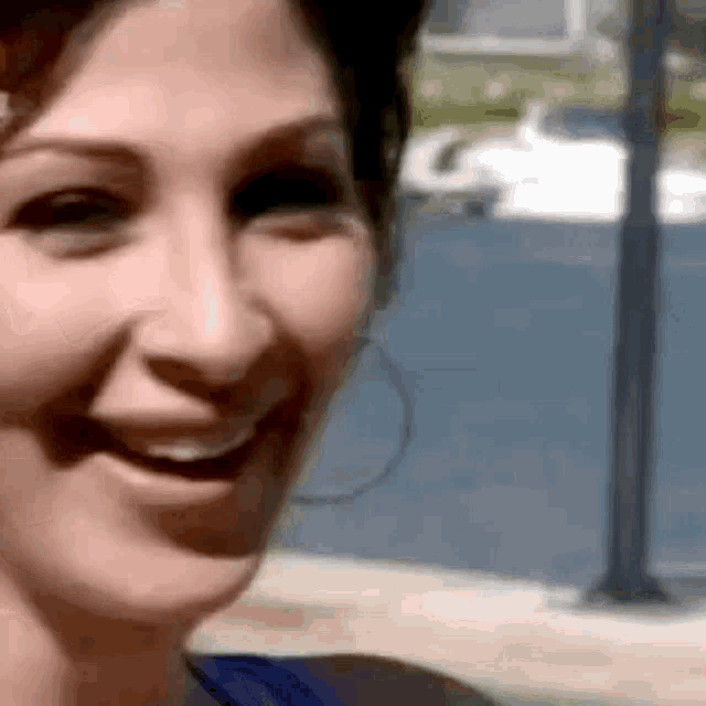 a close up of a woman 's face smiling with a tree in the background