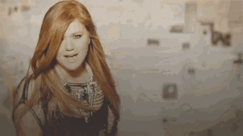 a woman with long red hair is standing in front of a wall with the letter m on it
