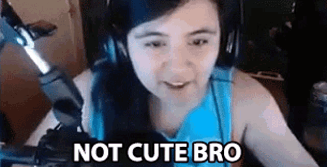 a woman wearing headphones is sitting in front of a microphone with the words `` not cute bro '' written on the screen .