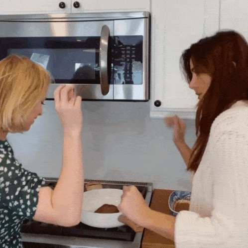 two women are cooking in front of a microwave that has the numbers 1 through 12 on it