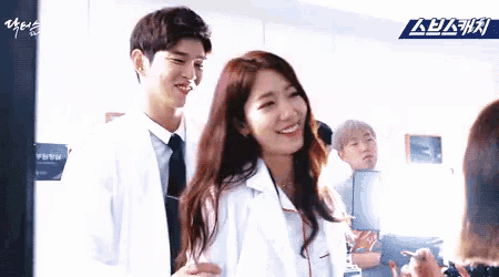 a man and a woman are standing next to each other and smiling . the woman is wearing a lab coat .