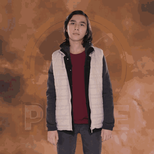 a young man in a red shirt and a white vest stands in front of a cloudy background with the letter p on it