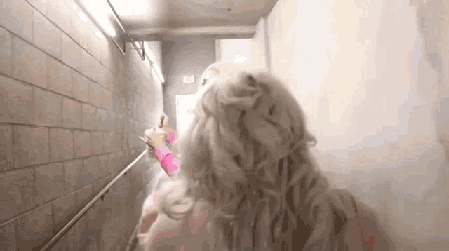 a woman with blonde hair is walking down stairs in a hallway .