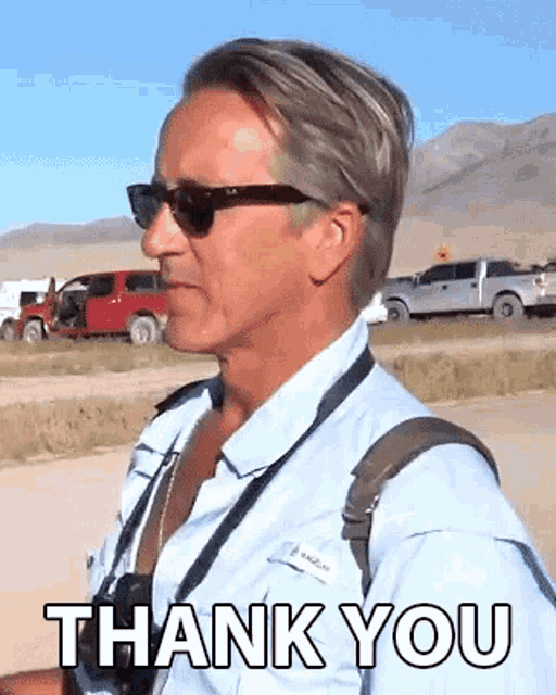 a man wearing sunglasses and a blue shirt is standing in front of a sign that says thank you .