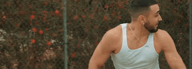 a man with a beard wearing a white tank top and a chain around his neck