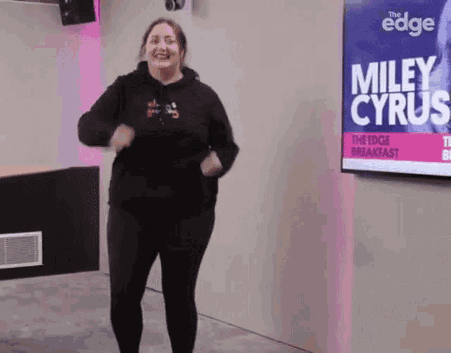 a woman is dancing in front of a screen that says miley cyrus